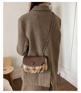 Detail of vintage plaid saddle bag with brown leather flap and silver chain strap on model