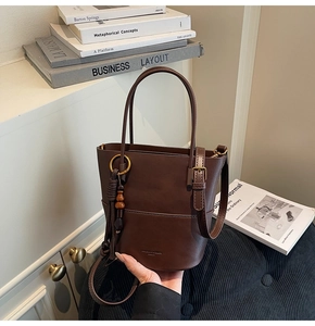 Detail of dark brown bucket bag featuring a wooden bead tassel and smooth leather texture
