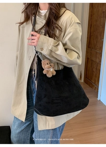 Close-up of minimalist black suede tote bag with a plush bear charm on a female model