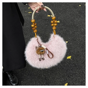 Fuzzy pink crescent bag with wooden bead handle and monster charm on fallen leaves