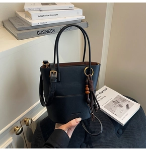 Detail of black bucket bag with matte texture, wooden bead charm and gold hardware