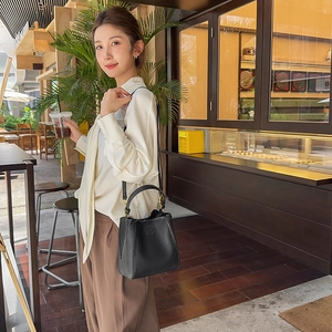 Close-up of black lychee-grain leather bucket bag with gold hardware in outdoor cafe setting