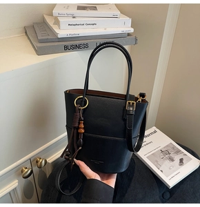 Detail of black matte bucket bag with golden hardware and wooden bead tassel accessory