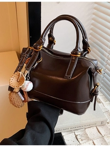 Retro brown leather Boston bag with white stitching and decorative charms on books