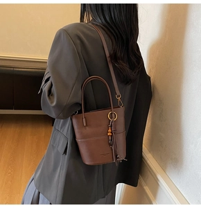 Detailed side view of a dark coffee bucket bag with stylish tassel and bead charm