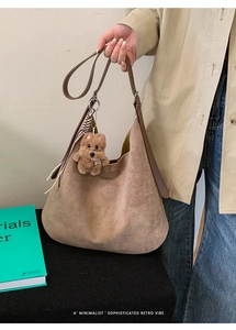 Detailed view of brown suede hobo bag with a cute plush charm and slim shoulder strap
