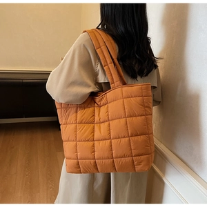 Detail of quilted puffer tote bag in vibrant orange featuring large grid stitching pattern