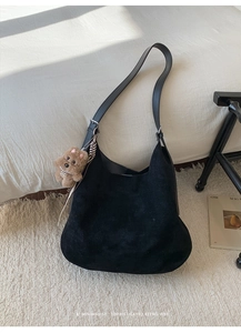 Detail of a minimalist black suede hobo bag with a cute brown plush dog charm accessory
