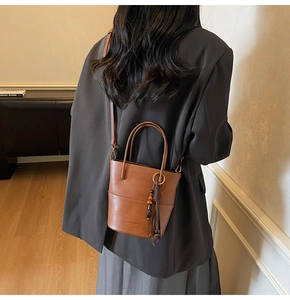 Detailed back view of a brown leather bucket bag with top handle and tassel on a model