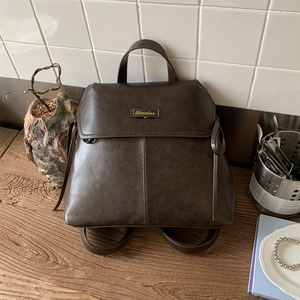 Detail of dark brown leather backpack with gold logo, flip-top design and side leather straps