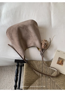 Detail of a brown faux suede tote bag with a plush bear charm on white bedding