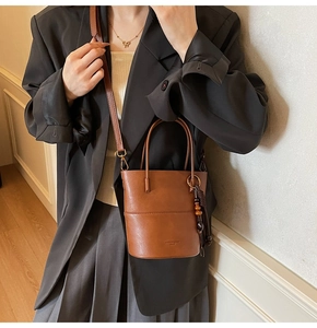 Close-up of brown bucket bag with tassel charm and adjustable strap held by model