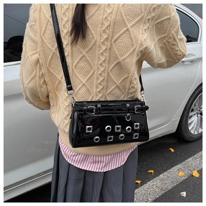 Detail of black patent leather crossbody bag featuring silver metallic eyelets and studs