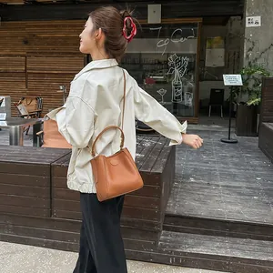 Brown leather bucket bag with pebble texture and adjustable strap in outdoor street setting