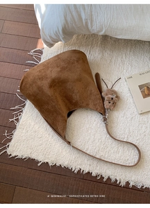 Detail shot of brown suede tote bag with plush bear charm on white fringed carpet