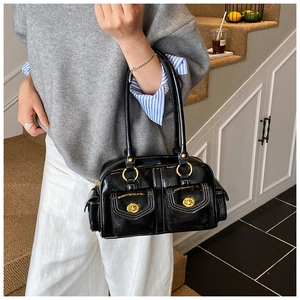 Detail of black glossy leather shoulder bag with white contrast stitching and gold buckles