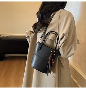 Detail of a black matte leather bucket bag with a wooden bead tassel on a model's shoulder