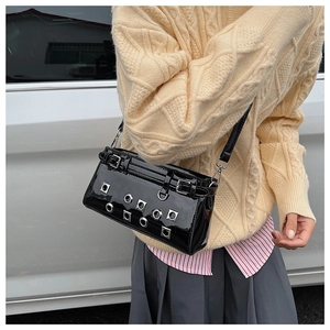Close-up of black glossy patent leather crossbody bag with silver eyelets and metal rivets