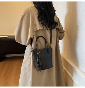Detail of black leather bucket bag with wooden bead tassel and crossbody strap