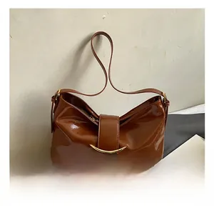 Détail du sac bandoulière marron brillant avec boucle en métal doré sur surface blanche