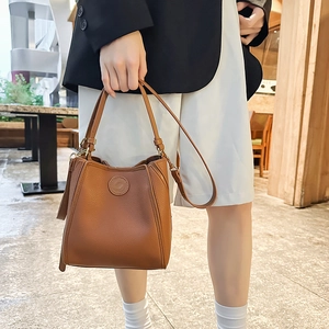 Detailed view of brown litchi grain leather bucket bag with top handle and gold hardware