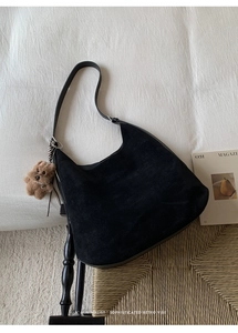 Detail of black suede hobo bag with a plush bear charm on a vintage sofa