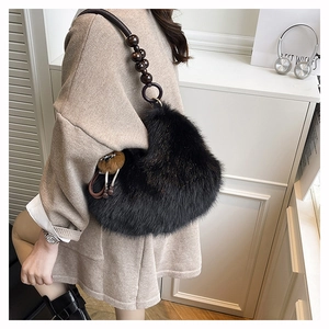 Detail of black plush handbag with wooden bead strap and brown pom-pom charm