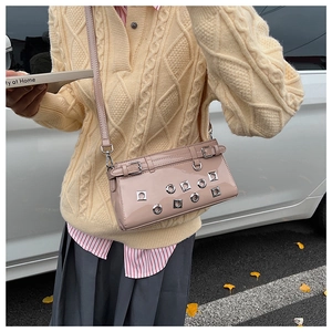 Pink faux leather punk crossbody bag with silver eyelets held by model in street setting