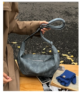 Close-up of grayish blue leather shoulder bag with zipper and wide strap in autumn setting