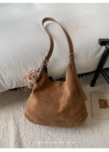Close-up of brown suede hobo bag with teddy bear charm on minimalist white rug
