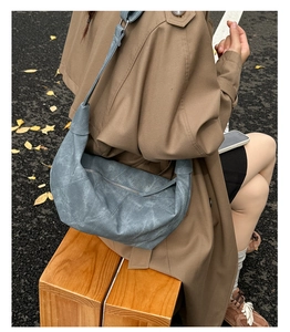 Suede moon-shaped crossbody bag worn by a model in a trench coat on a park bench