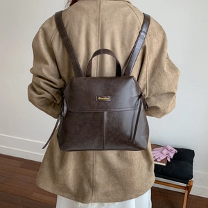 Detail showing vintage dark brown PU leather texture and premium metal logo on backpack