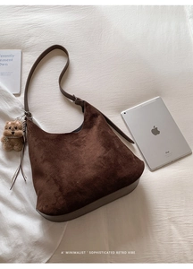 Detail view of a dark brown suede hobo bag with a cute plush bear charm on white bedding