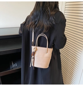 Model wearing a beige bucket bag with wooden bead tassel details from a back view perspective