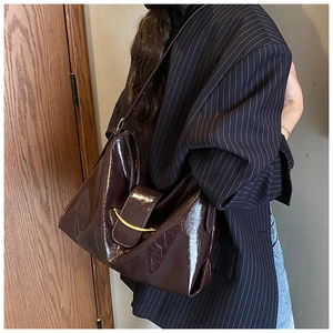 Détail du sac cabas en cuir verni marron brillant avec boucle en demi-lune dorée sur modèle