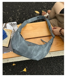 Detail of grey-blue Hobo bag with vintage texture and adjustable strap on a bench