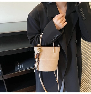 Close-up of minimalist beige bucket bag featuring a woven wooden bead and leather tassel