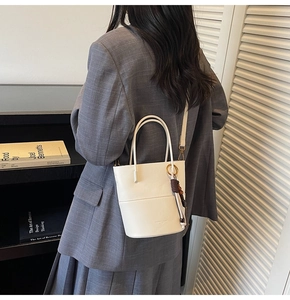 Cream bucket bag featuring circular top handles and a tassel with wooden beads detail