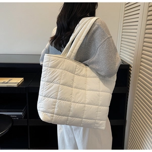 Detail view of white quilted puffer tote bag worn on shoulder in a modern room
