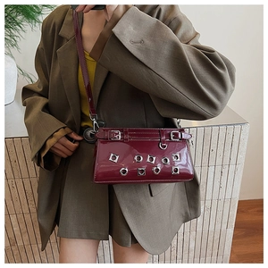 Detail of burgundy patent leather crossbody bag with metal eyelets and buckled straps
