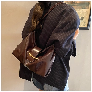 Détail du cabas en cuir verni café foncé avec boucle dorée en croissant sur le sac à main
