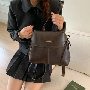 Detail of dark brown faux leather bag with gold logo and adjustable shoulder strap