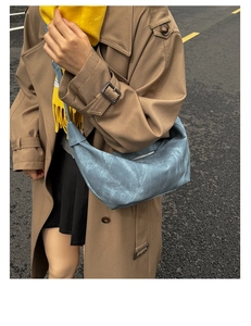 Detail of light blue crescent bag with distressed texture on trench coat model