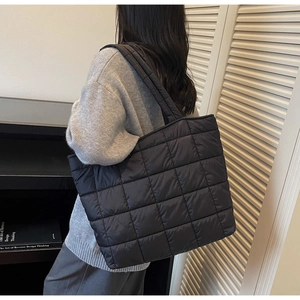 Model wearing a black quilted puffer tote bag with wide shoulder straps in a side view