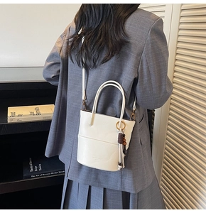 Close-up of a white leather bucket bag with a detachable strap and decorative tassel charm
