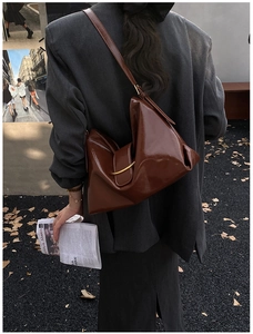 Détail d'un sac cabas marron foncé brillant avec pliage asymétrique et boucles dorées