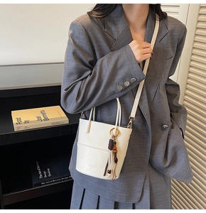 Close-up of white bucket bag with leather tassels and adjustable strap in lifestyle setting