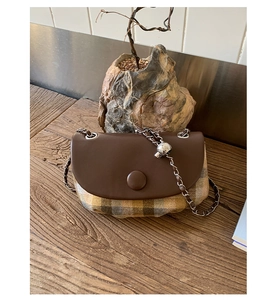 Detail of vintage plaid saddle bag with brown leather flap and silver chain strap