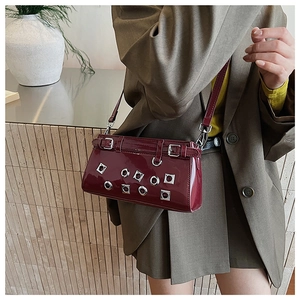 Detail of dark red patent leather bag with silver metal eyelets and adjustable buckle