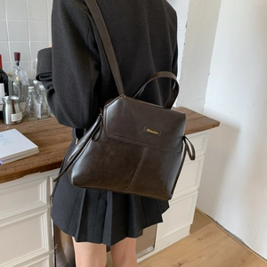 Detail of a vintage dark brown PU leather backpack with top handle and metal branding